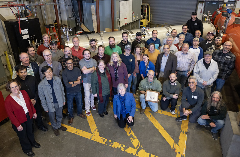 Jefferson Lab contributors to the Spallation Neutron Source Proton Power Upgrade pose for a photo with CM-08, final cryomodule produced for the project.