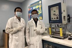 Researchers Haodong Liu and Ping Liu hold batteries made with the disordered rocksalt anode material they discovered, standing in front of a device used to fabricate battery pouch cells. (credit: UC San Diego)